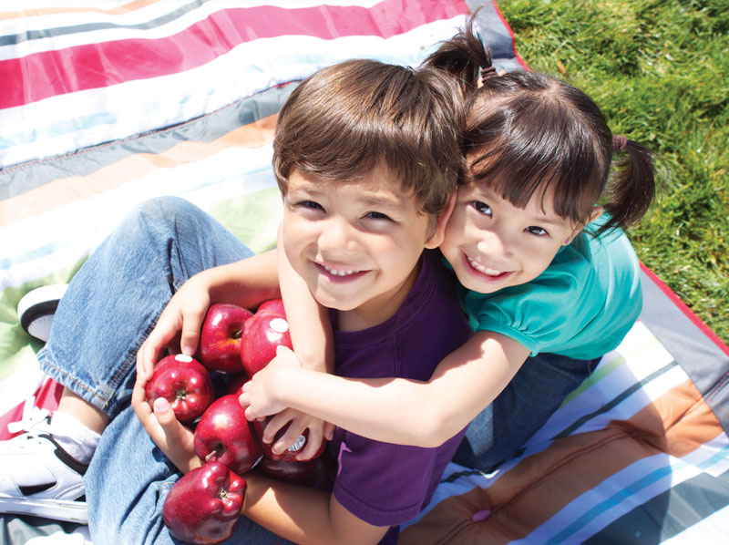 Young boy and girl hugging and holding apples.